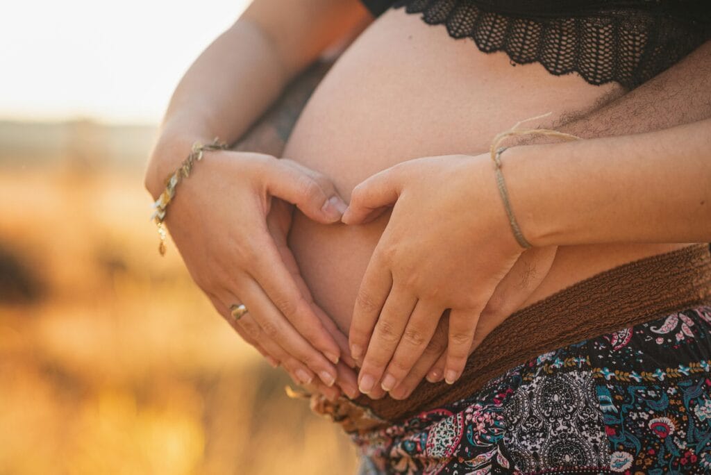 Close-up of a couple's hands forming a heart over a pregnant belly, symbolizing love and family.