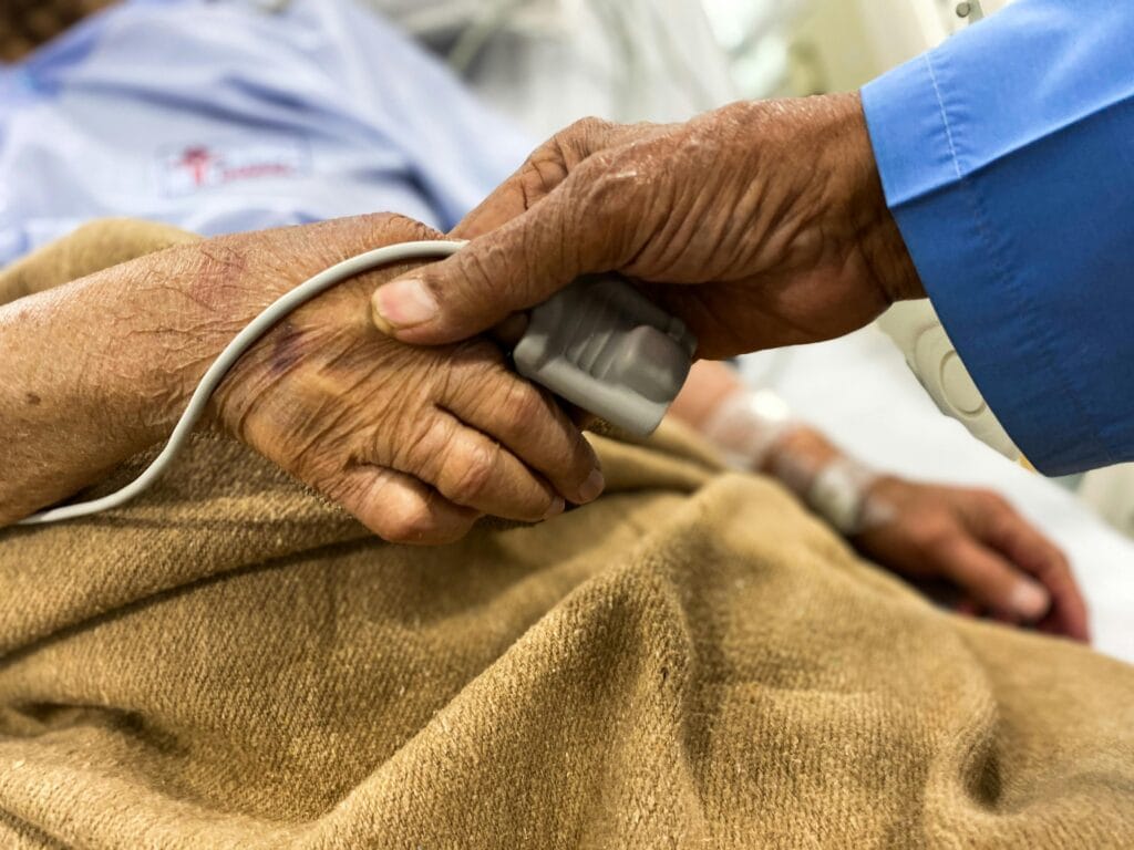 pexels-photo-3934328-3934328-1 Crop old female patient lying on medical bed with pulse oximeter on finger and old man holding wrinkled hand