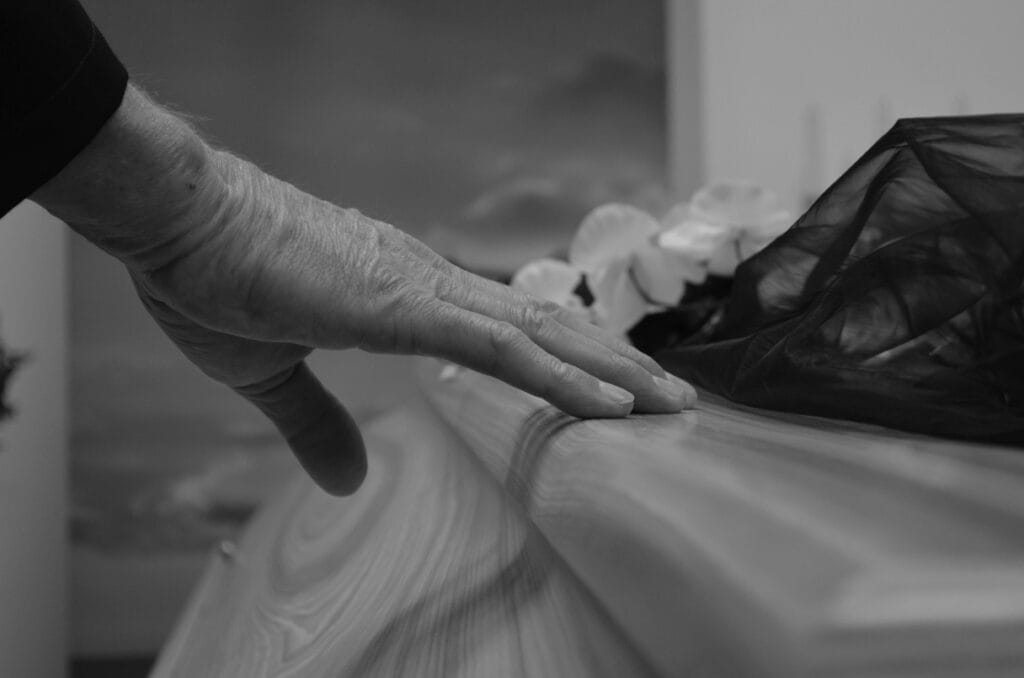 pexels-photo-9563478-9563478-1 A touching black and white image of a hand resting on a coffin, symbolizing a final farewell.