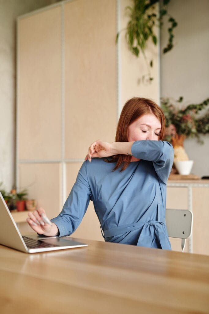 Woman covers mouth sneezing in office setting, illustrating common cold symptoms.